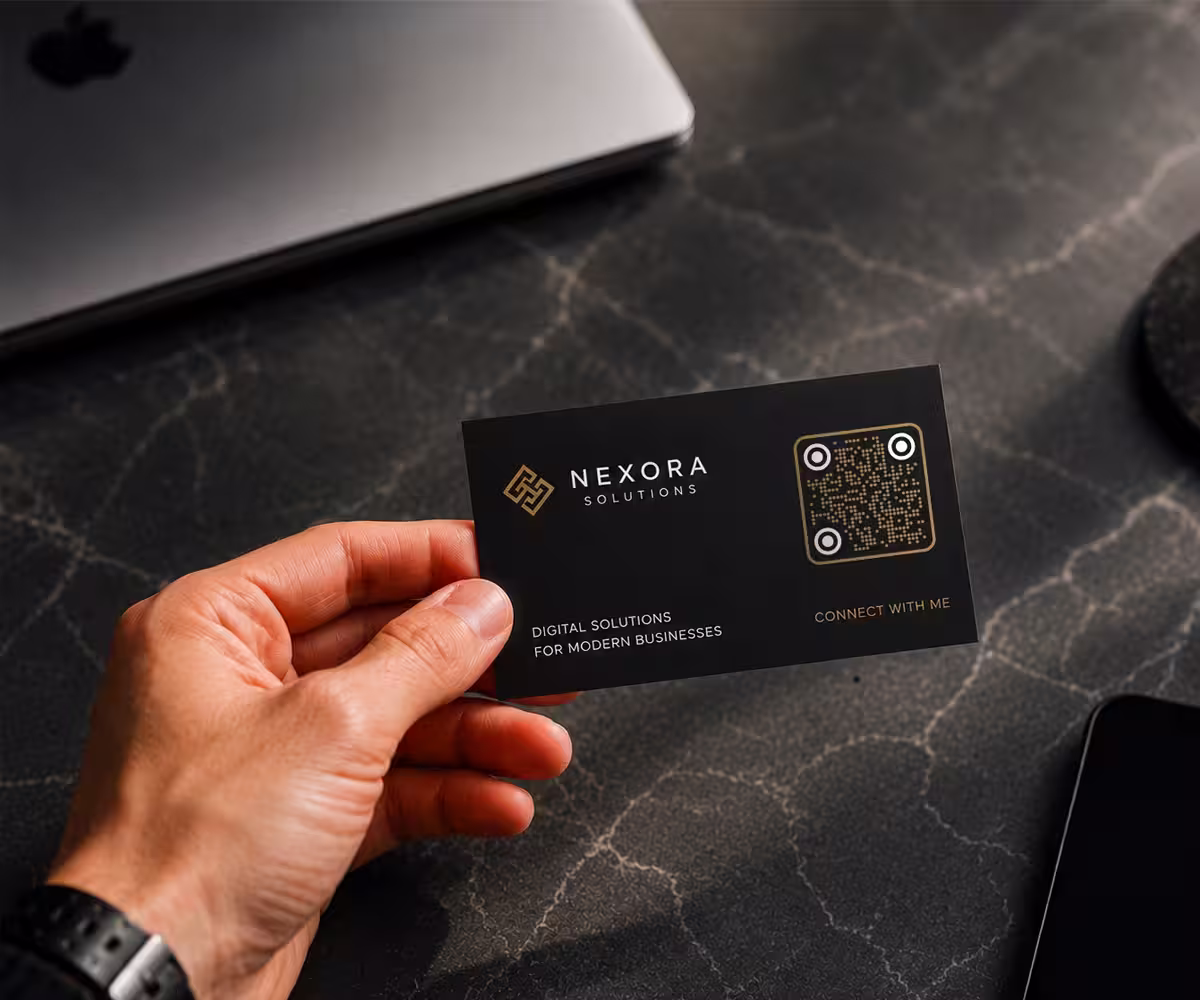A hand holding a business card with a gold QR code printed on it